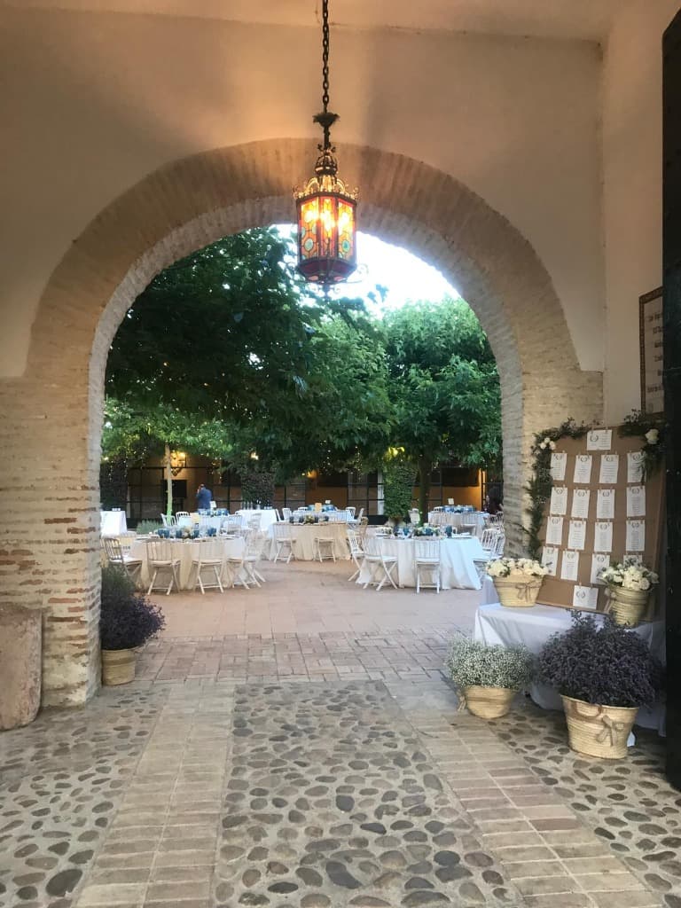 Entrada Patio Banquete Bodas Entrada por arco de piedra hacia el patio del banquete de bodas con seating plan en Sevilla
